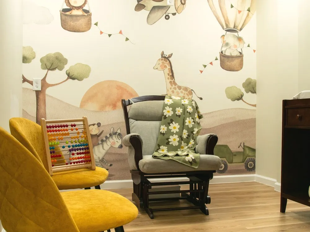Infant care room with a giraffe mural and nursing glider